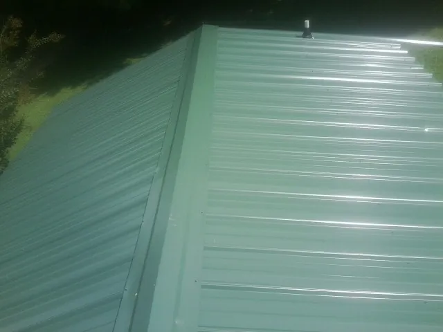 New green metal panels meeting at the ridge of a roof — Flat Roof Repair work by our crew in La Crosse