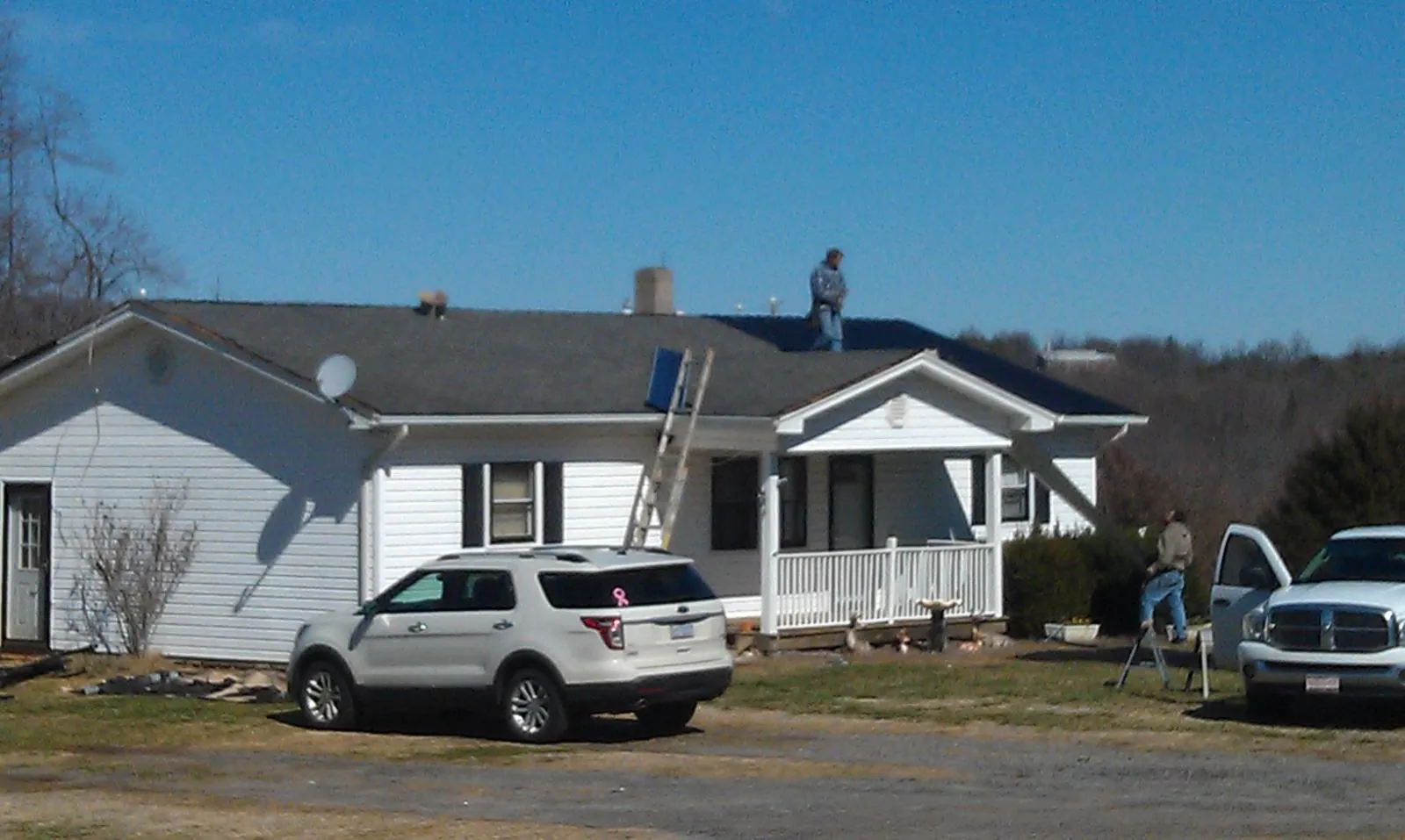 Roofers stripping shingles from a white ranch house roof in La Crosse